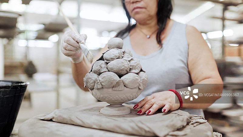 工人在陶瓷厂用刷子给华丽的雕像上釉图片素材