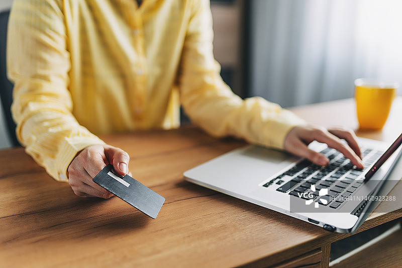 年轻女子在家坐在地板上，用信用卡和笔记本电脑在网上购物的照片图片素材