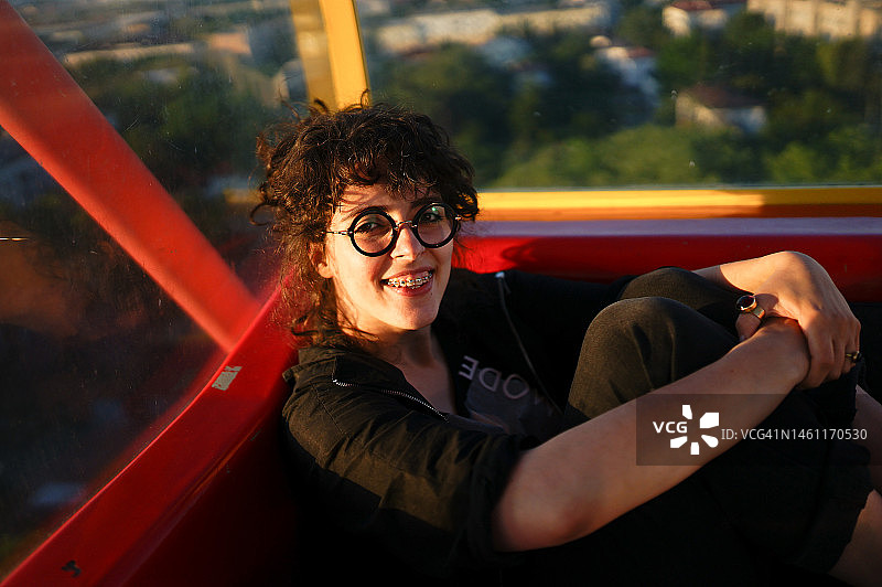 坐在摩天轮座舱里的笑容满面的卷发戴眼镜的女人图片素材