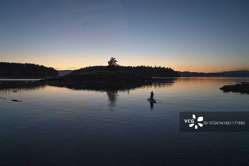 一人在黄昏时分站在岛屿之间的桨板上图片素材