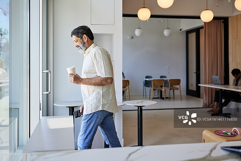 拿着一次性咖啡杯离开咖啡店的微笑中年男人图片素材
