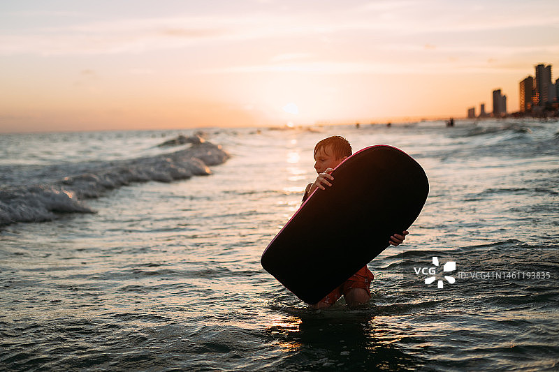 日落时分在海滩上拿着滑板的男孩图片素材