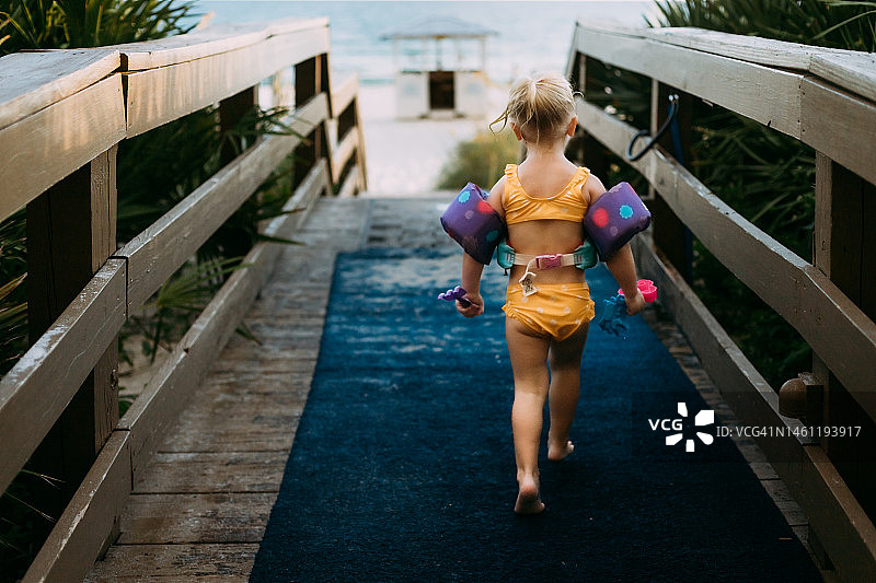 年轻女孩走在通往海滩的木板路上图片素材