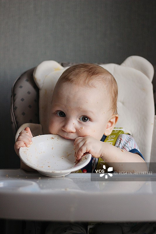 坐在餐椅上咬盘子的小男孩图片素材