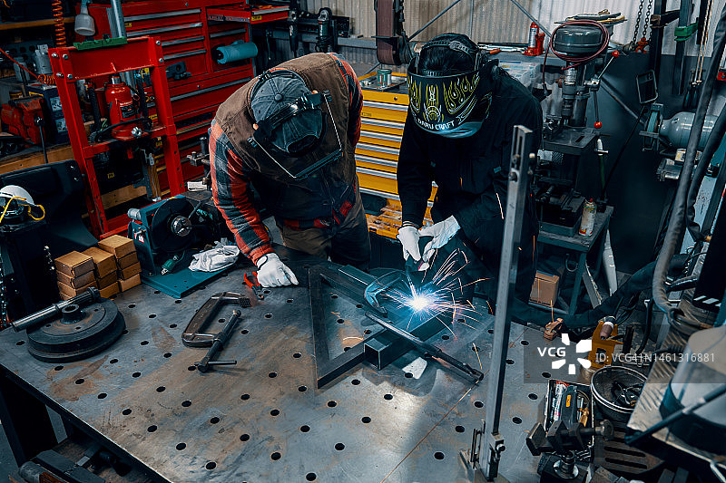 中年男人在金属制造车间教女员工焊接图片素材