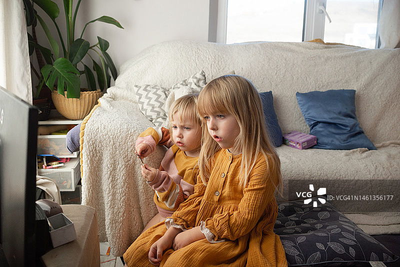 孩子们在家里的沙发上看电视或电脑上的动画片图片素材