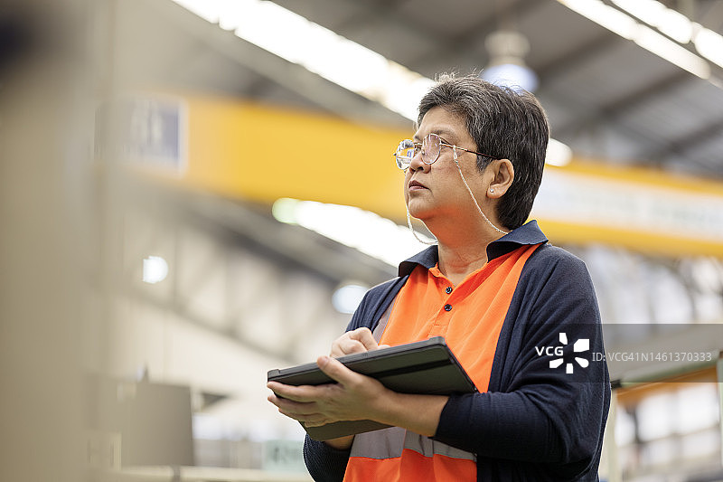 企业质量保证，确保产品质量，让客户满意。亚洲女性工厂经理手持平板电脑在生产线上检查生产过程，以提高质量。图片素材