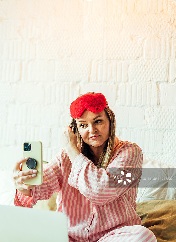 戴眼罩在床上玩手机的女人图片素材