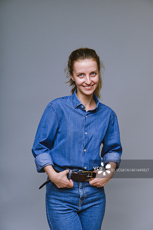 穿着牛仔裤服装，手扶皮革腰带的快乐女子图片素材