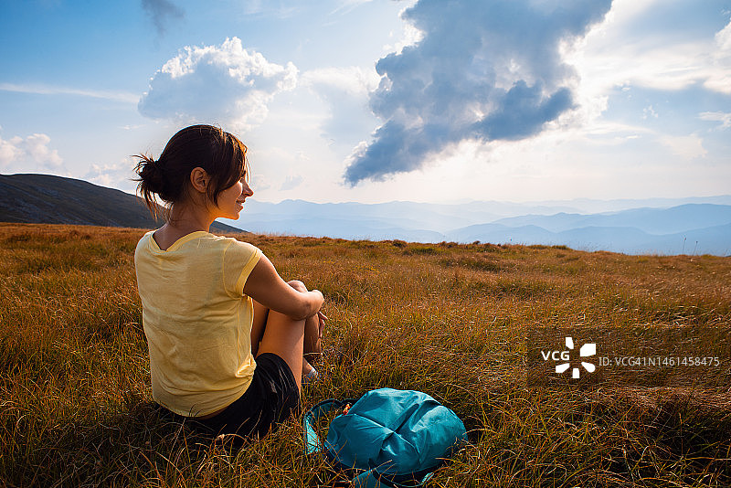 徒步旅行者在日落时分坐在多云天空下的山顶上图片素材