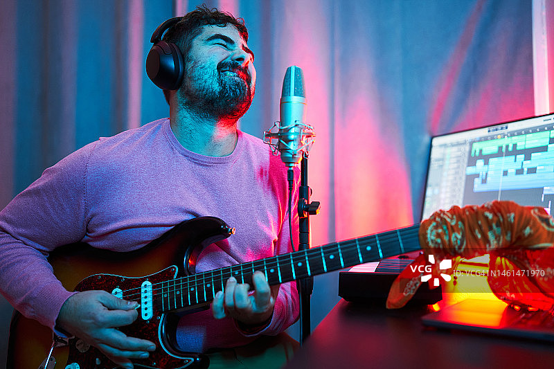 在家庭音乐工作室里唱歌和弹电吉他的快乐男人图片素材
