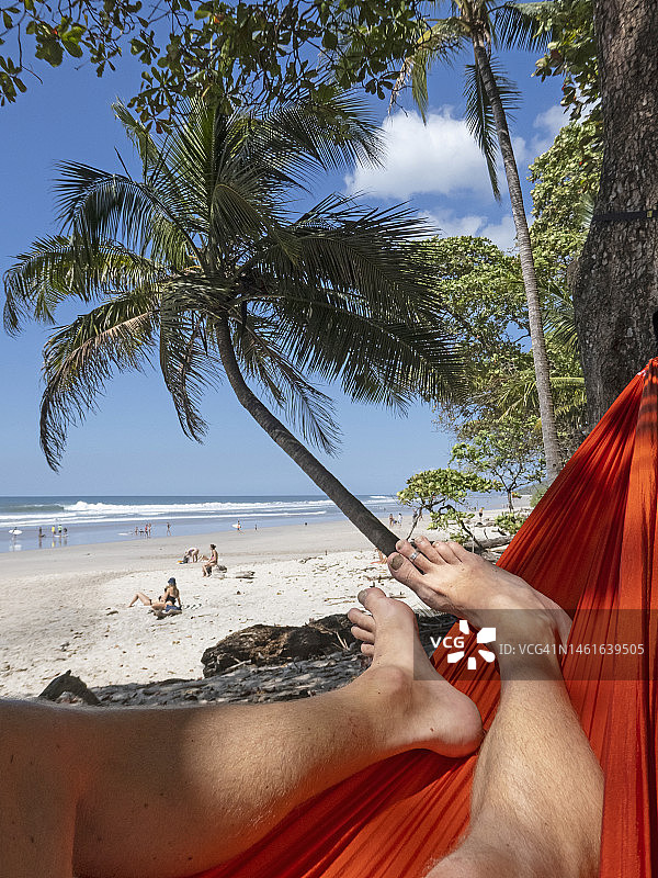 男子在海滩的橙色吊床上放松图片素材