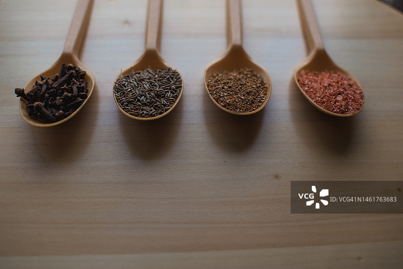 木制背景上的香料勺：孜然、丁香、盐、胡椒图片素材