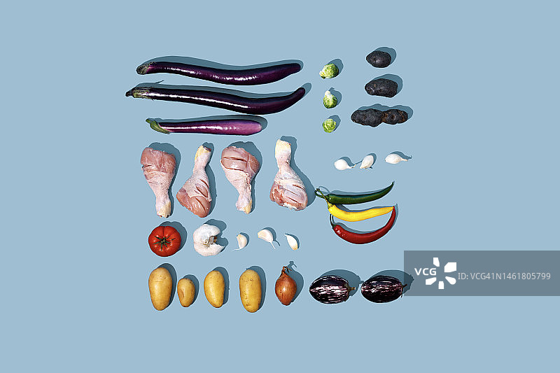 蓝色背景上的生鸡腿、土豆、紫土豆、茄子、大蒜、洋葱、胡椒、柠檬和西红柿 - 食物摆拍图片素材