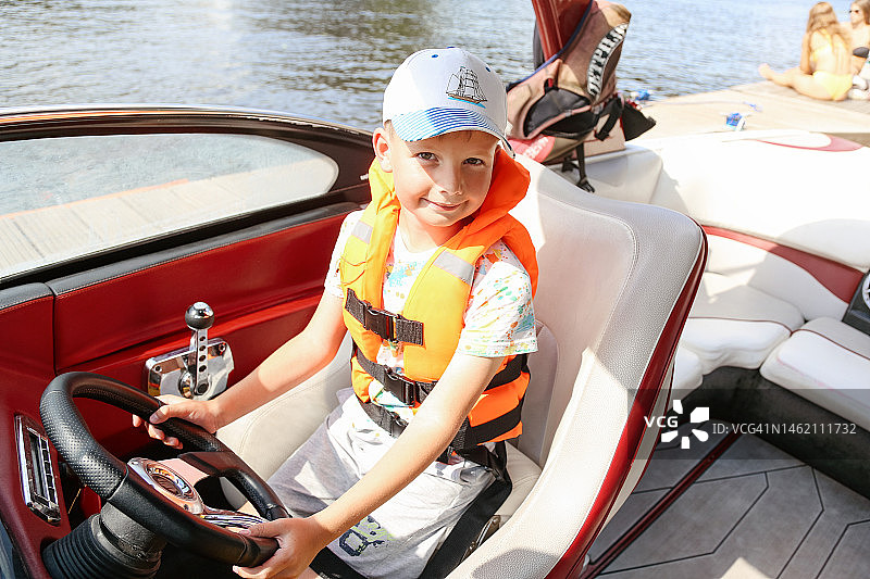 勇敢的男孩穿着橙色救生衣练习驾驶快艇图片素材