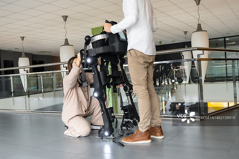 机械外骨骼：现代医院的物理治疗，理疗师和科学家在康复室外准备机器人骨骼，科学家、工程师和理疗康复医生使用平板电脑进行辅助图片素材