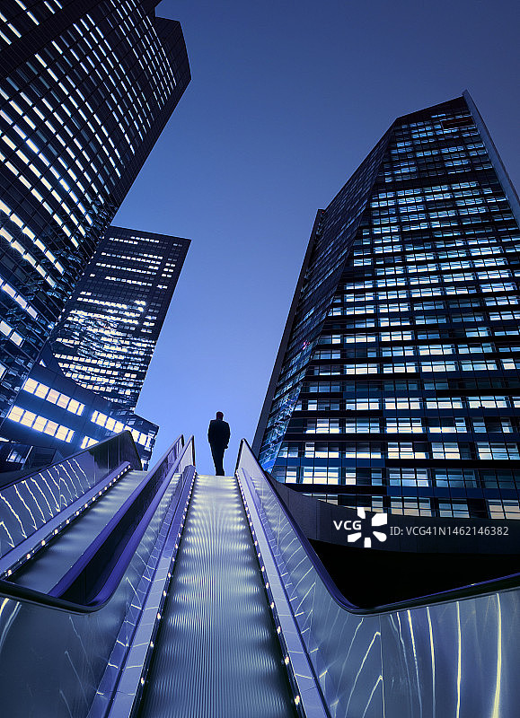 在灯火通明的商业区乘坐自动扶梯的商务人士图片素材