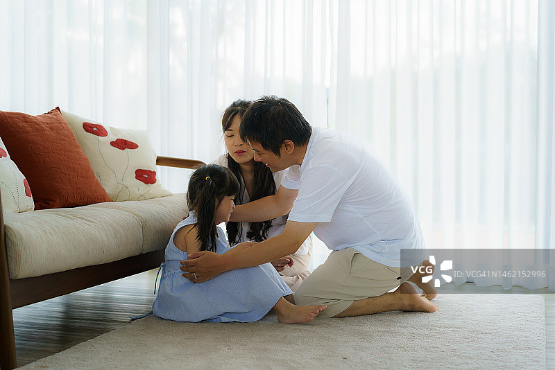 亚洲父母拥抱在客厅里哭泣的孩子，表达家庭之间的身体感情概念图片素材