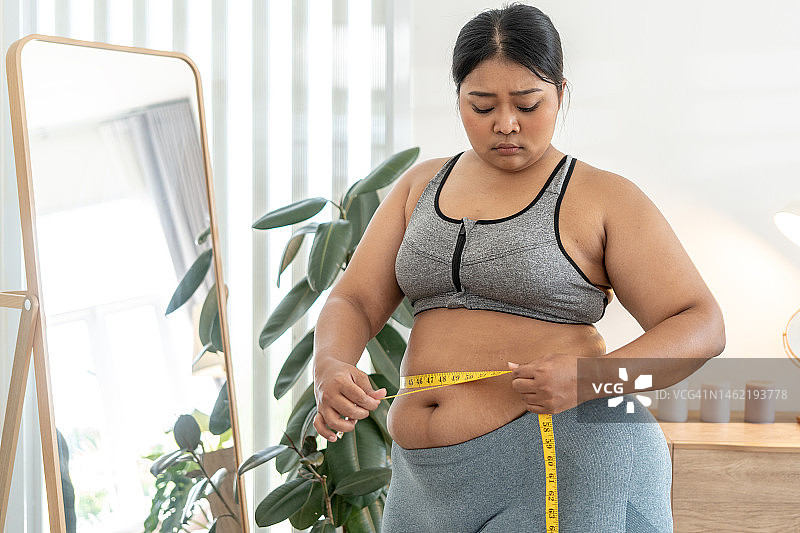 站在镜子前量腰围的胖女人图片素材