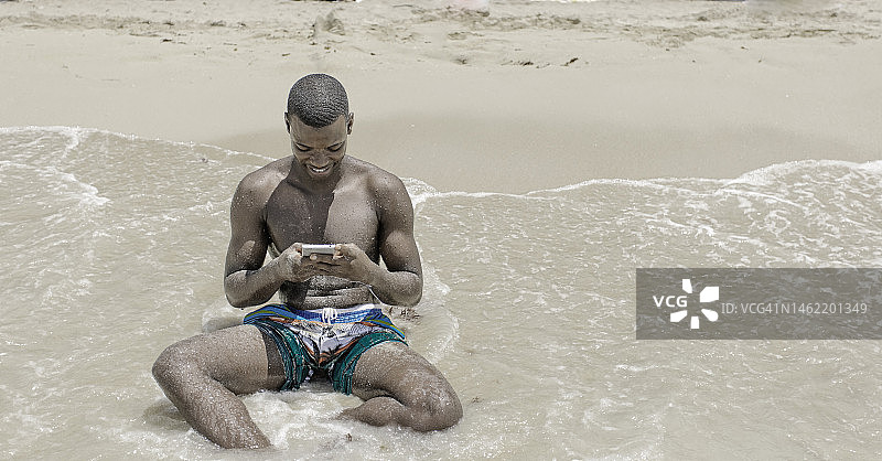 非裔美国男子在海浪附近使用智能手机图片素材