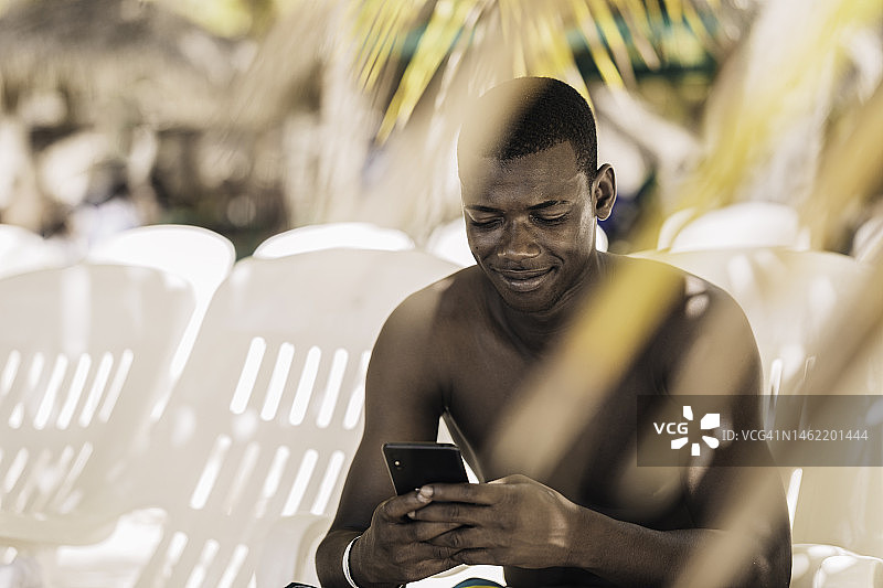 快乐的黑人男子在海滩上使用智能手机图片素材