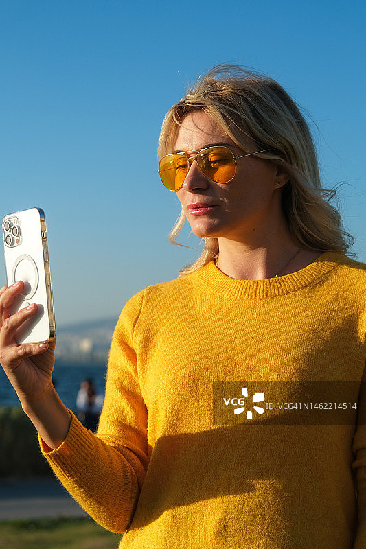 在市中心草地上使用手机的金发女人图片素材