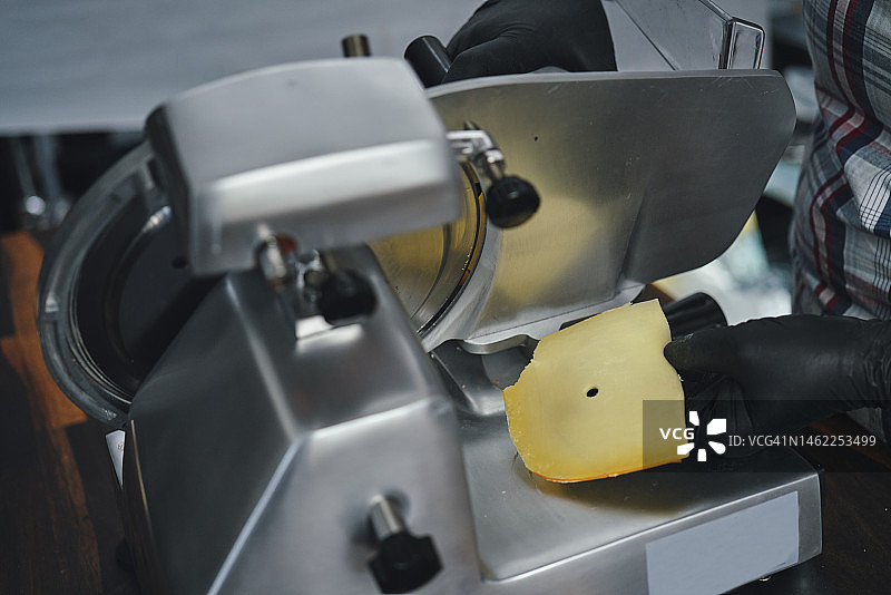 食品安全 - 戴着食品手套在切片机上切奶酪图片素材