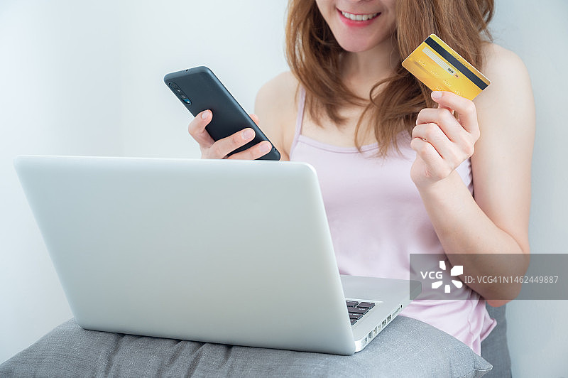 女人手持信用卡和智能手机在笔记本电脑上进行网上购物图片素材