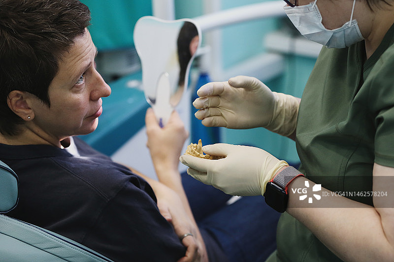 成年女牙科医生制作牙科修复体并展示给焦虑的病人图片素材
