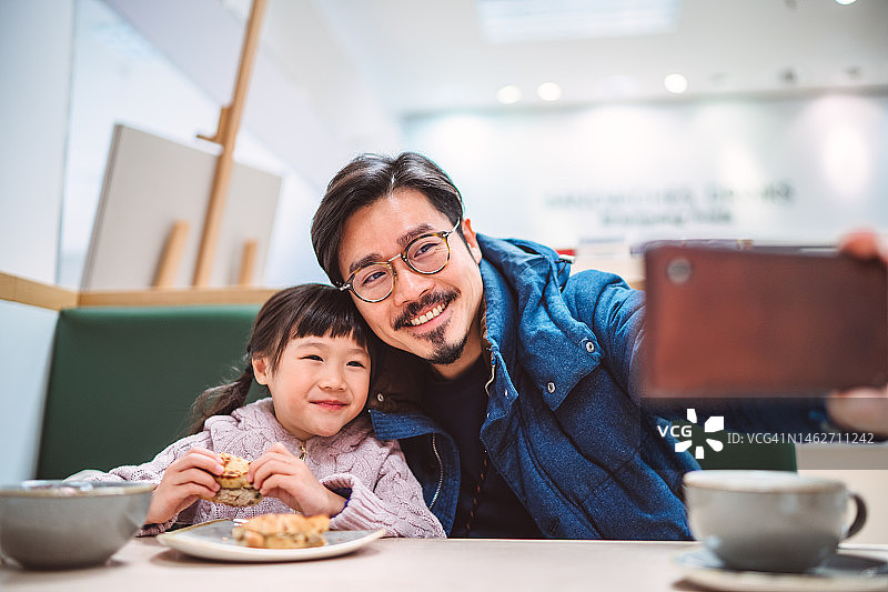 父亲和女儿在餐厅用餐时用智能手机自拍图片素材