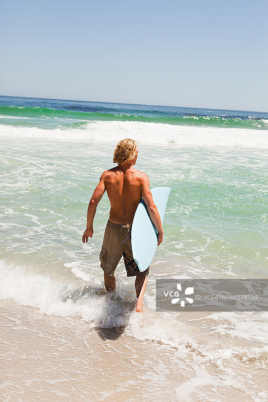 年轻金发男人拿着冲浪板在水中行走图片素材