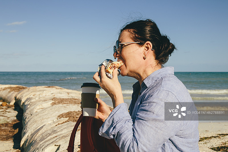 在海滩上吃三明治的中年妇女图片素材