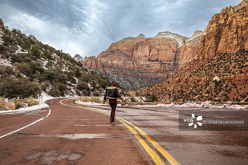冬季峡谷地貌中，在山路上欣赏美丽自然风光的年轻女人图片素材