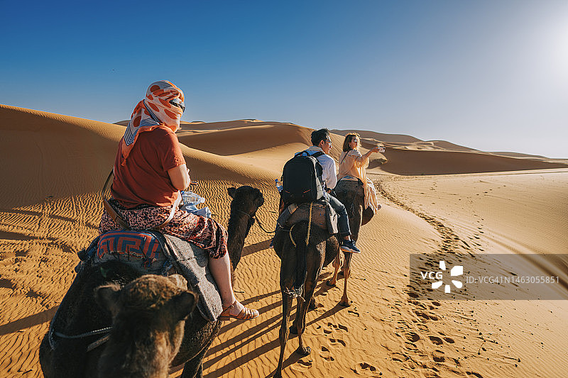中国游客骑着单峰骆驼穿过摩洛哥撒哈拉沙漠图片素材