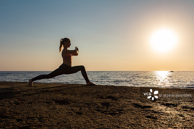 战士瑜伽姿势——年轻瑜伽女性在海边户外练习图片素材
