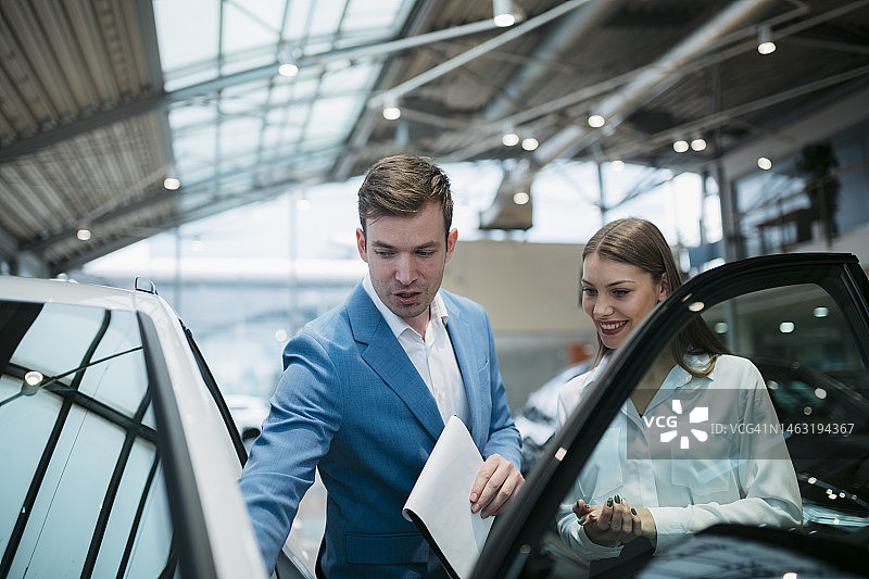 汽车经销店里的销售经理向女顾客展示汽车图片素材