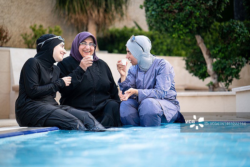 快乐的穆斯林女性在泳池边喝咖啡图片素材