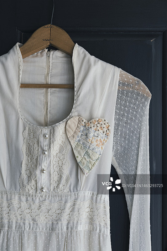 复古浪漫的连衣裙挂在木制衣架上，胸前别着绗缝心图片素材