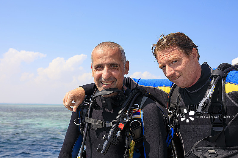 中年运动员的好朋友，两名英俊的男子潜水员准备水肺潜水，背景是美丽的热带蓝色海洋和珊瑚礁，水上运动图片素材