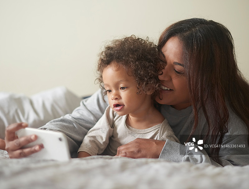 母亲在卧室床上用手机播放儿童娱乐节目图片素材