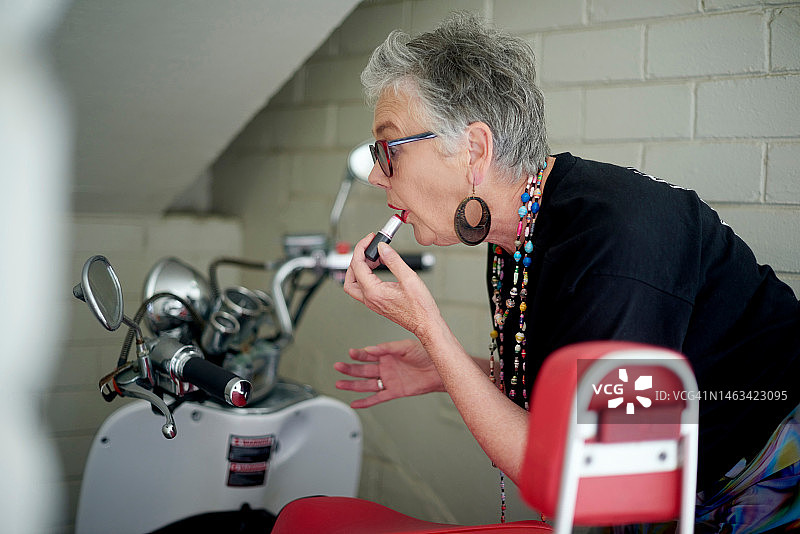 老年妇女骑摩托车，对着镜子涂口红，在旅行途中化妆图片素材
