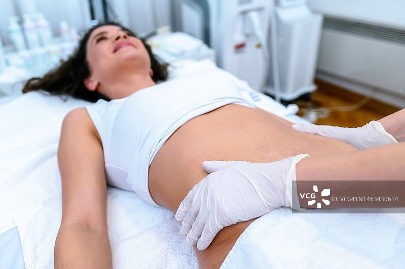 美容师为有妊娠纹的女士腹部涂抹乳霜图片素材