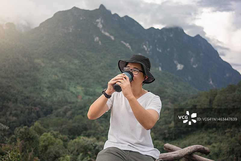 在郊野公园里拿着可重复使用咖啡杯微笑的年轻亚洲男人图片素材