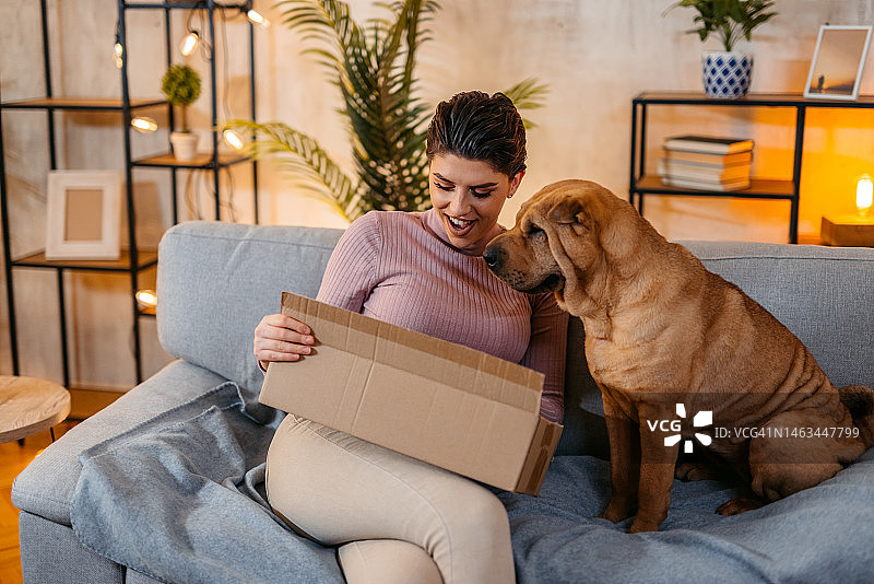 年轻女人和她的狗在拆开网上购买的包裹图片素材
