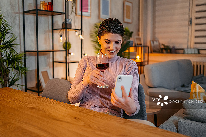 年轻女人在家喝酒并进行视频通话图片素材