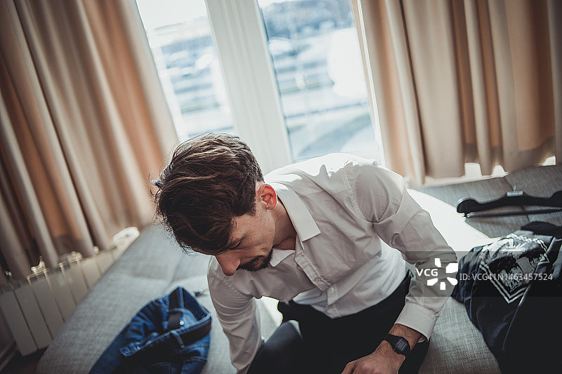 年轻的波兰男子在酒店房间里穿着白衬衫，用笔记本电脑在线工作图片素材