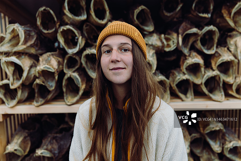 戴着黄色帽子站在罗弗敦群岛鳕鱼干前的妇女肖像图片素材