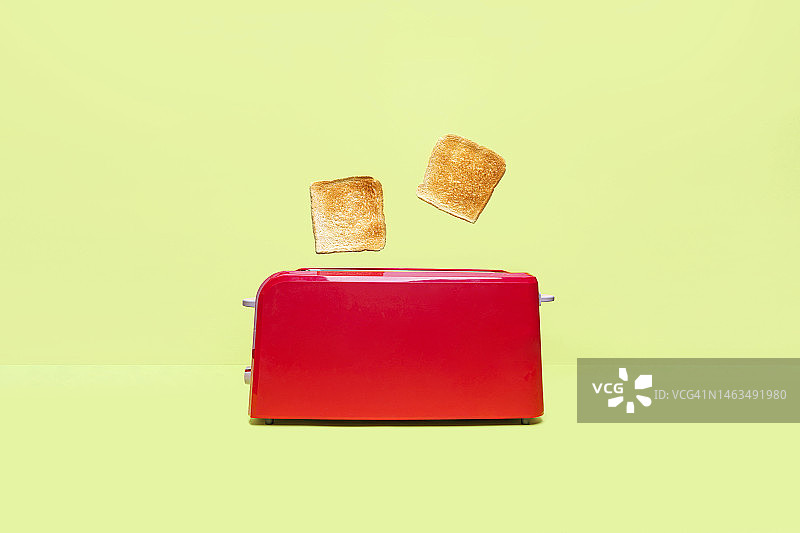 绿色背景上的红色烤面包机和两片新鲜吐司图片素材