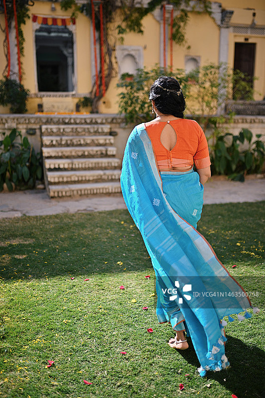 身穿纱丽的印度美丽女子在庭院中跑步的后视图图片素材
