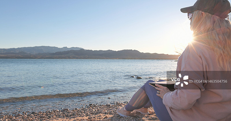中年妇女在湖边早晨使用笔记本电脑图片素材